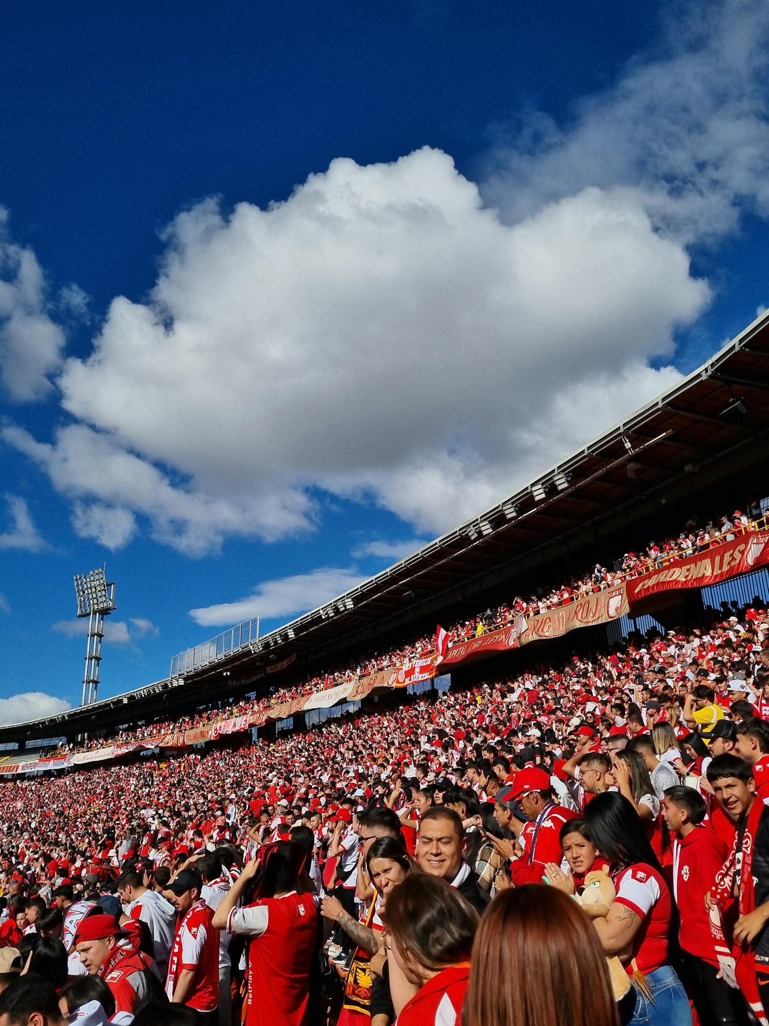 A lively crowd fills the Bogotá stadium under a vibrant blue sky.