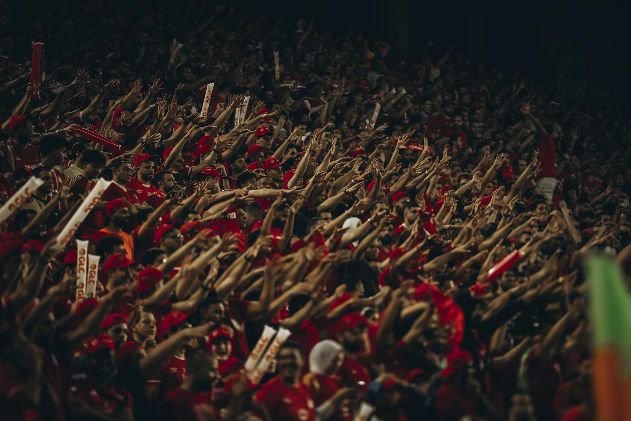 A vibrant crowd of football fans passionately cheering during a match at night.